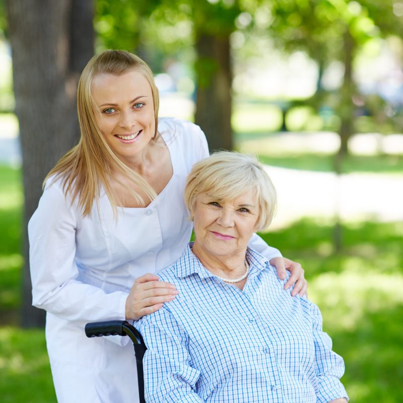 Pretty nurse and senior patient in a wheelchair looking at camera in park